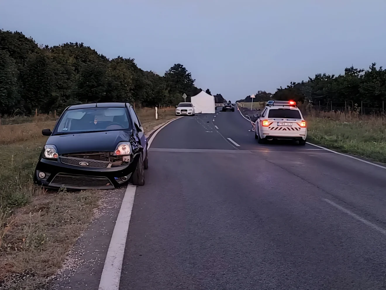 Rendőrautók és összetört személyautó a Veszprémet Szentkirályszabadjával összekötő úton, a halálos motorbaleset helyszínén.