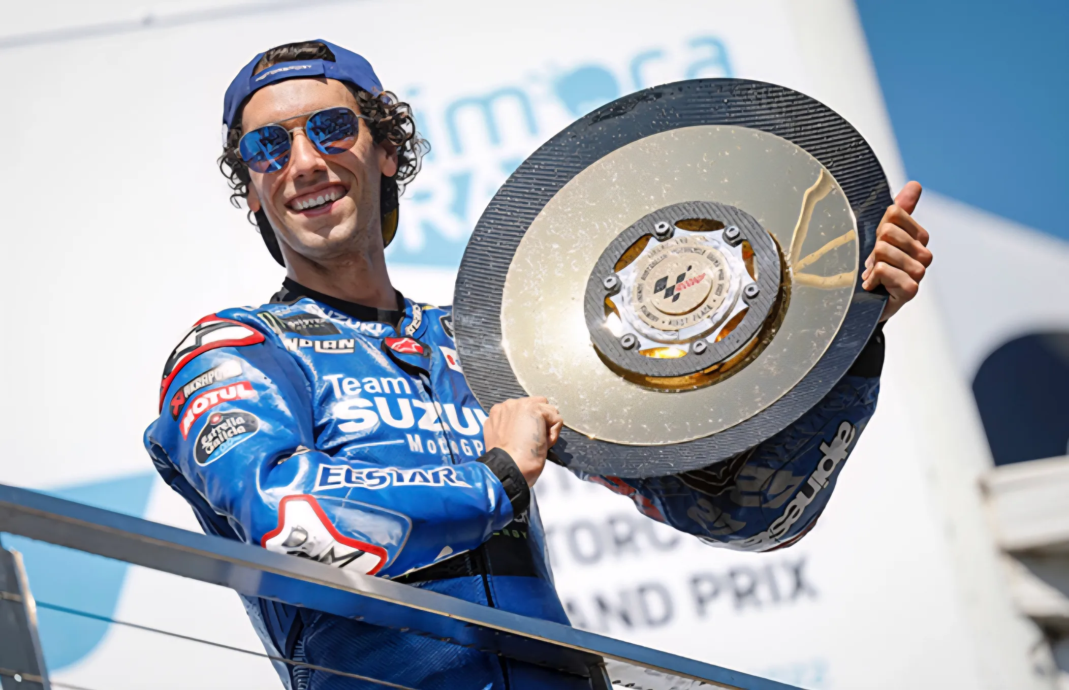 Alex Rins ünnepli MotoGP-győzelmét a Suzuki csapatával. Alex Rins a dobogón emeli a MotoGP-trófeát a Suzuki Ecstar színeiben ünneplés közben