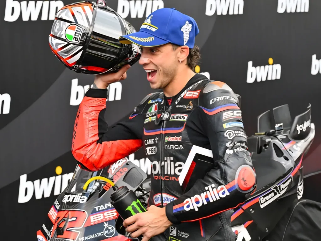 Marco Bezzecchi az Aprilia Racing motorja mellett sisakját a magasba emelve ünnepli MotoGP-győzelmét.